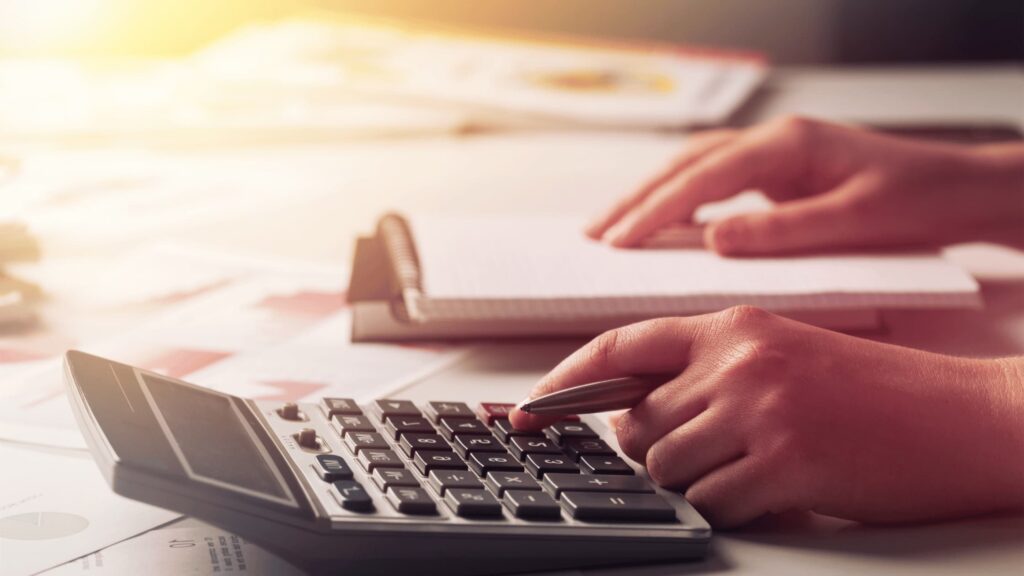 Person using a calculator and taking notes on a desk