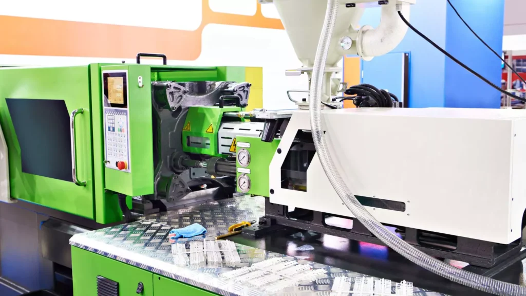 A green and white automated injection molding machine with a control panel and a hopper for feeding plastic material, producing plastic components.