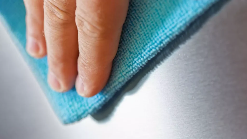 A close-up of a hand using a blue microfiber cloth to clean a smooth stainless steel surface, ensuring a polished finish.