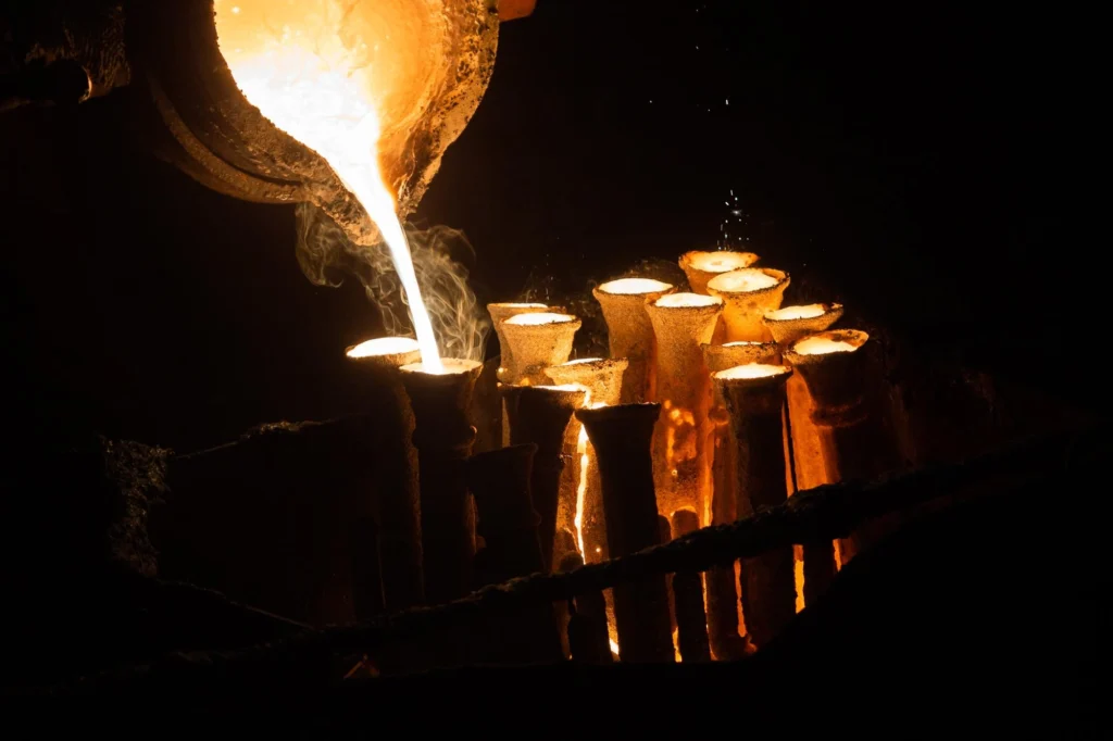 Glowing molten metal being poured into multiple cylindrical molds in a dark industrial setting.