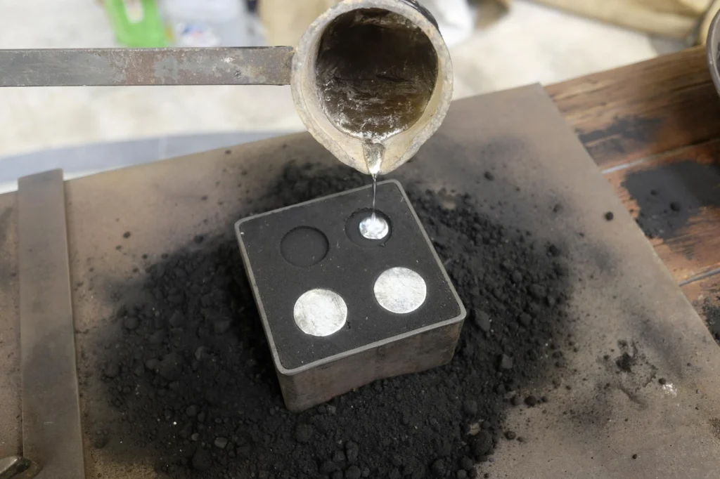 Molten metal being poured into small circular molds, highlighting a precise casting process.