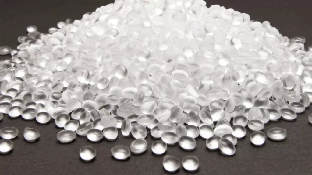 A close-up image of transparent plastic pellets, the raw material used in injection molding processes, displayed on a dark surface