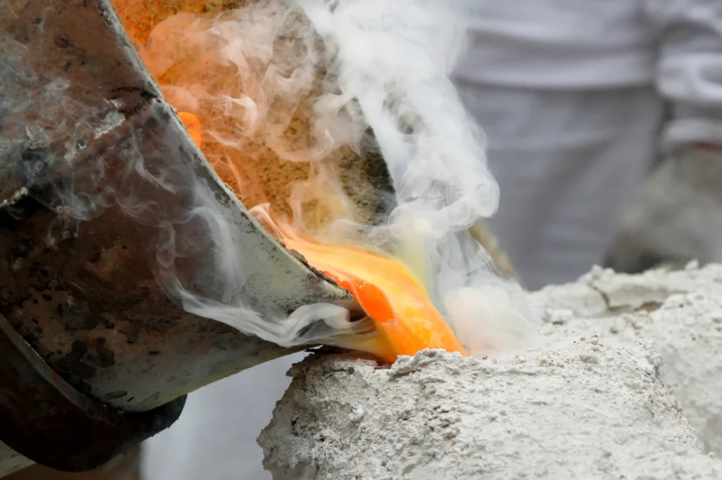 Molten metal being poured into a mold with smoke rising, illustrating the dynamic and intense casting process.