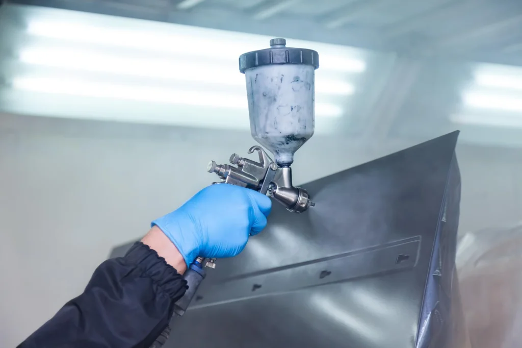 A technician using a spray gun to paint a metal surface, ensuring a smooth and even coating.