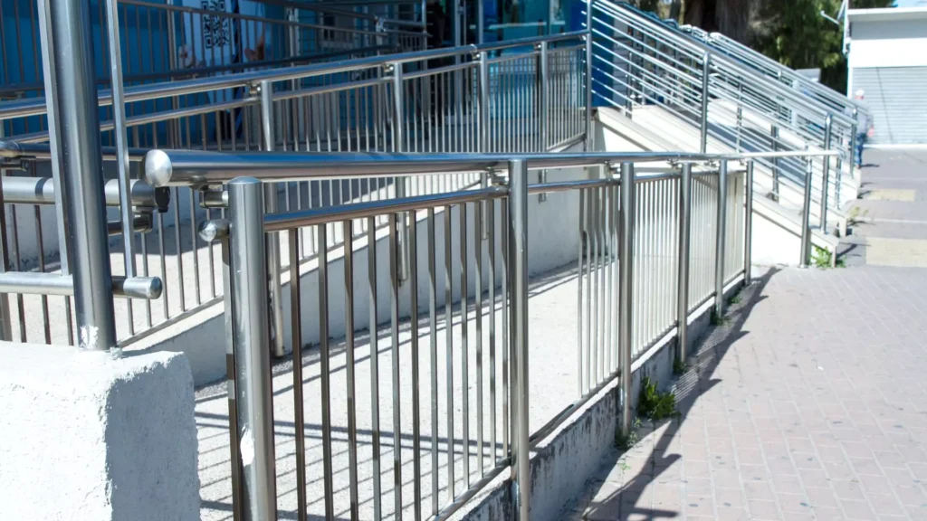 A series of stainless steel handrails along an outdoor ramp, providing accessibility and safety in a public area.