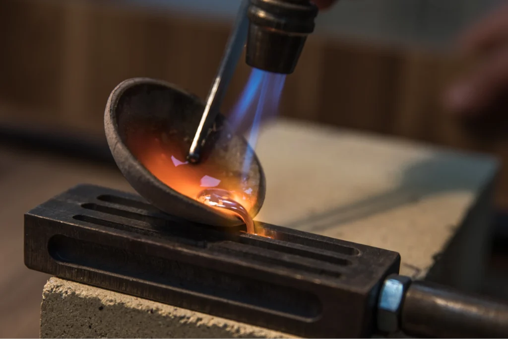 A blowtorch heating a small crucible of molten metal for crafting and shaping purposes.