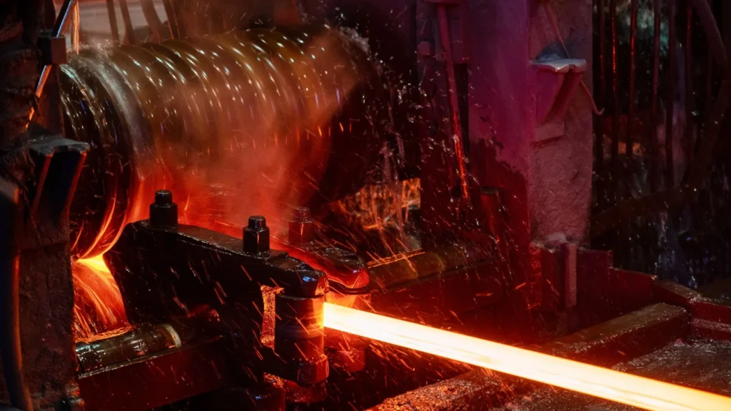 A high-temperature hot rolling process where glowing red-hot steel is being shaped through industrial rollers, with sparks and cooling water splashes.