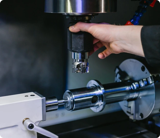 A close-up of a CNC machine in operation, with a technician adjusting the cutting tool while machining a metal component